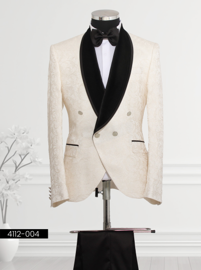 Ivory and black tuxedo featuring floral brocade patterns, black velvet shawl lapel design, double-breasted closure with silver buttons, matching bow tie, and tailored trousers.