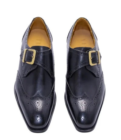 Black monk strap shoes with brogue detailing, gold buckle, pointed toe, and tan interior.
